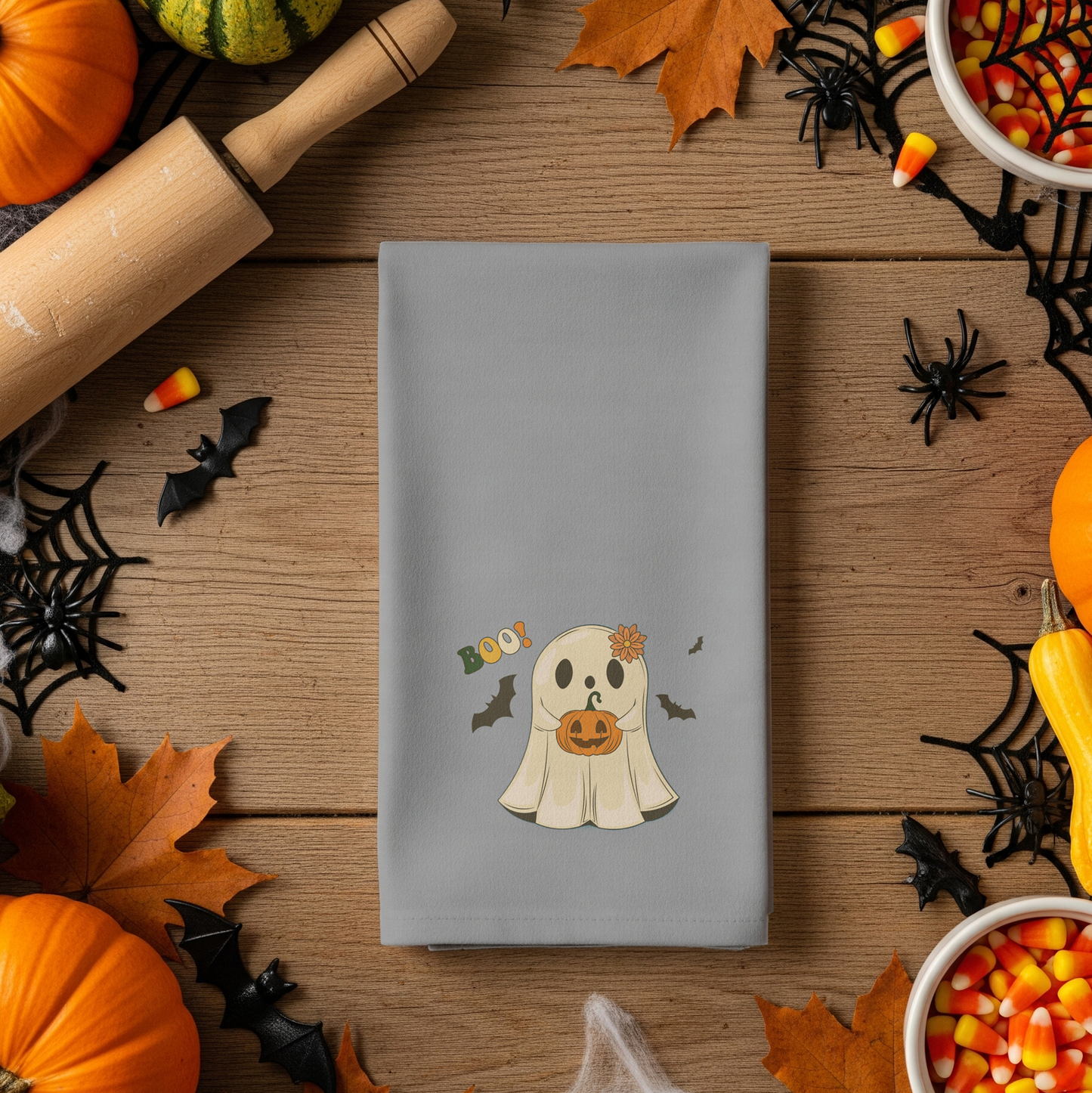 Gray napkin with a ghost design surrounded by Halloween decorations on a wooden table.