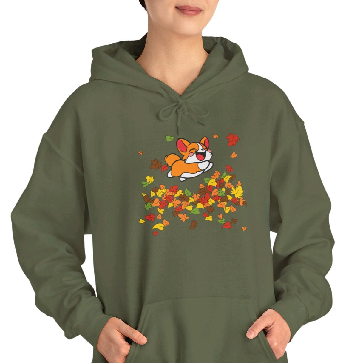 A woman wearing a green hoodie with a graphic of a corgi dog surrounded by autumn leaves.