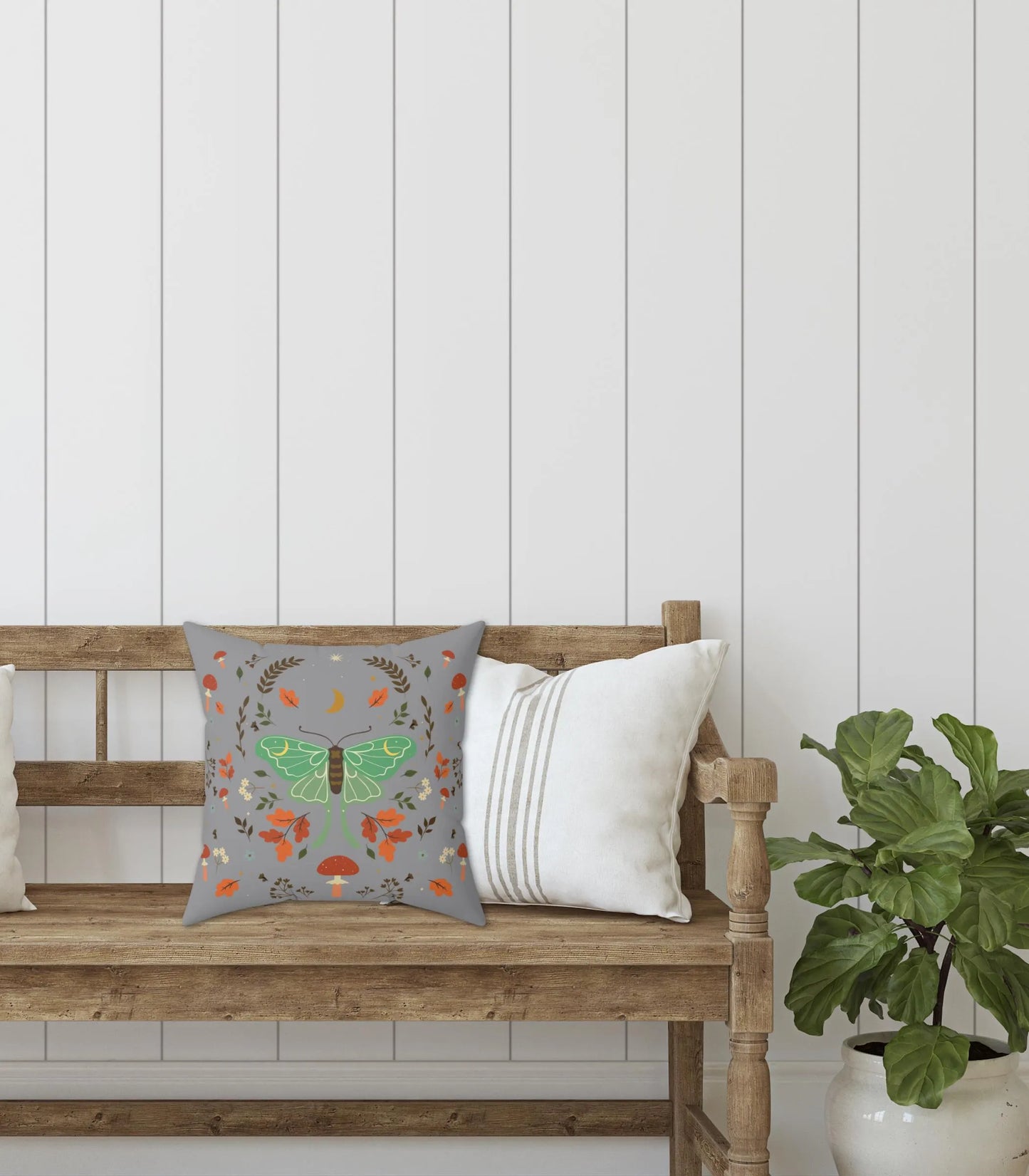 Decorative pillow with a luna moth design on a wooden bench against a white paneled wall.