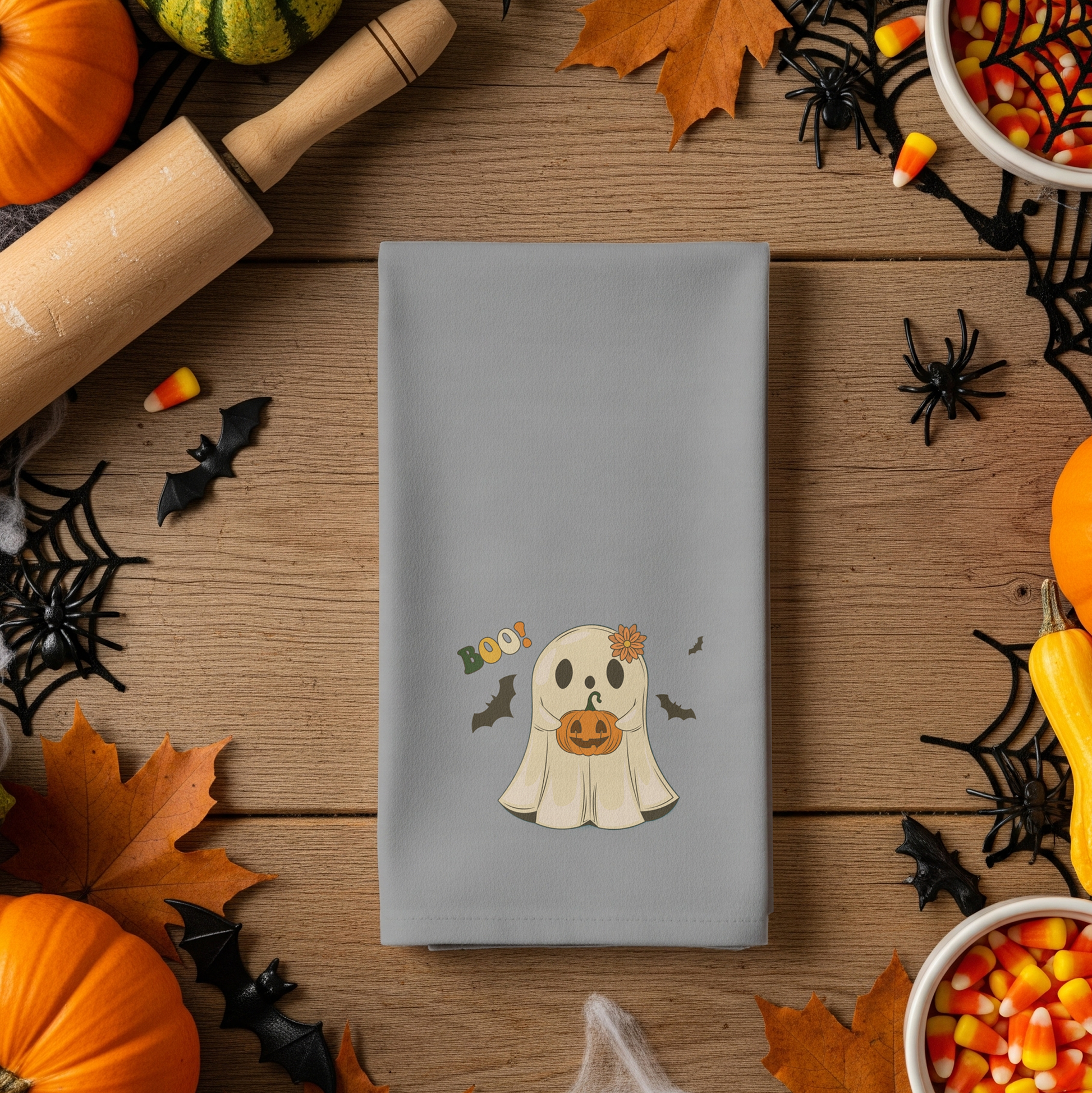 Gray napkin with a ghost design surrounded by Halloween decorations on a wooden table.