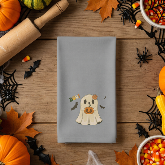 Gray napkin with a ghost design surrounded by Halloween decorations on a wooden table.