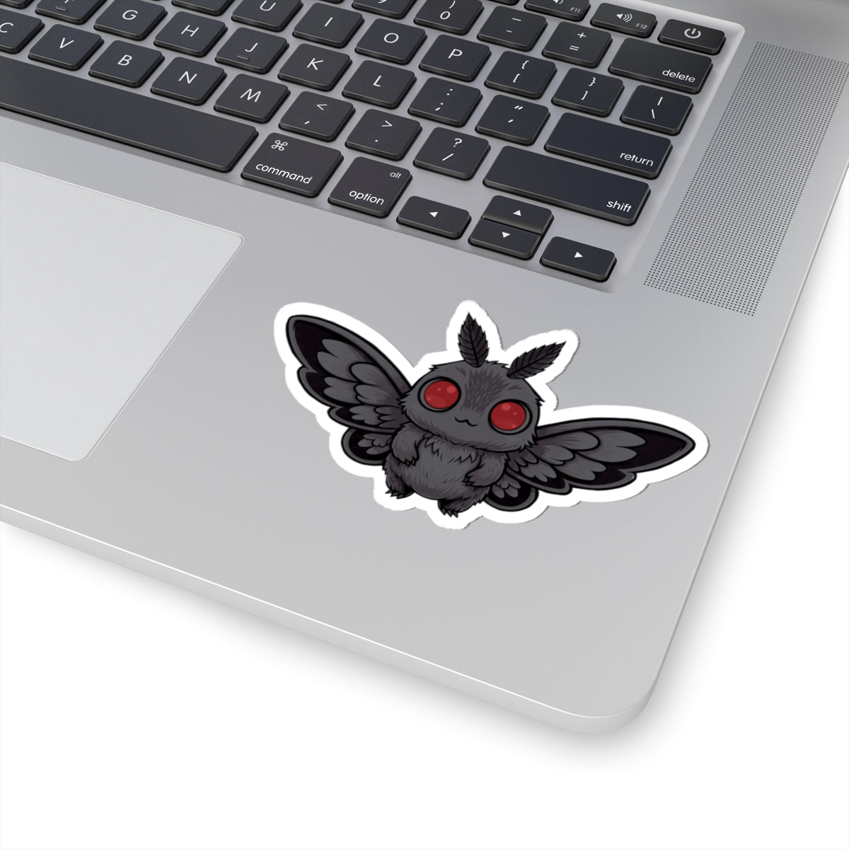 Laptop with a sticker of a black creature with red eyes on the palm rest area.